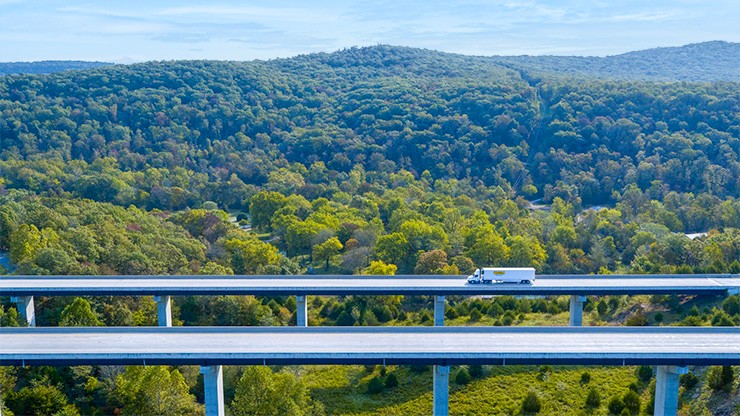 wide shot of truck on highway green trees